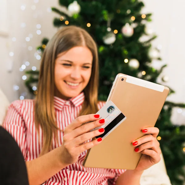 A woman holds a credit card and a tablet, exploring options for a Christmas loan.
