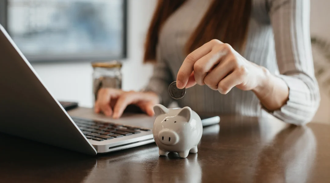 Woman placing a coin into a piggy bank on a desk, symbolizing borrowing to invest for future financial growth.