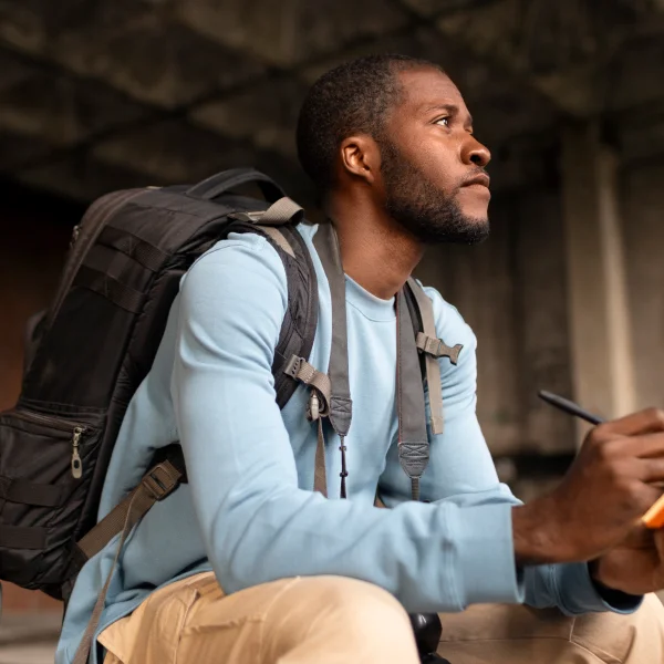 Un homme assis par terre avec un sac à dos, prêt à voyager pour vivre des expériences mémorables.