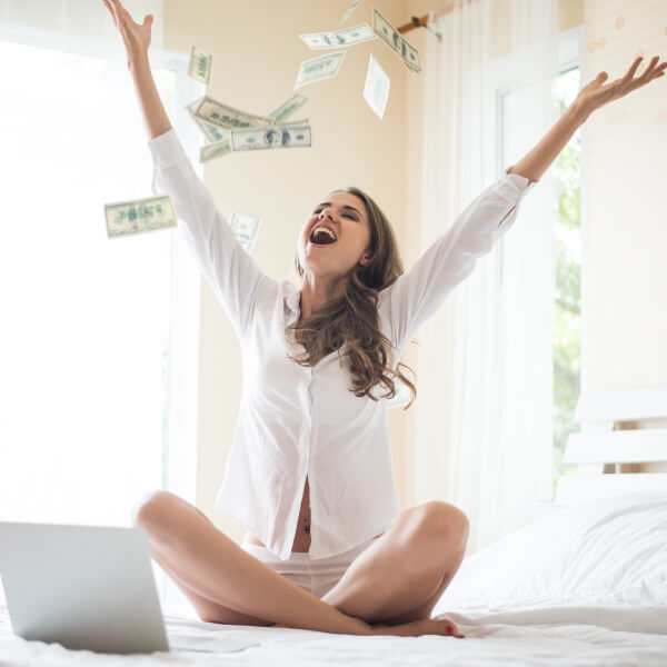 A woman sits on a bed as money falls from the ceiling, illustrating how a small loan can create significant impact.
