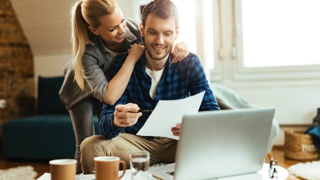 Une vue en plongée d'un professionnel travaillant tard le soir, interagissant avec un ordinateur portable, une tablette et un smartphone affichant des graphiques, illustrant le rythme rapide des besoins financiers modernes.